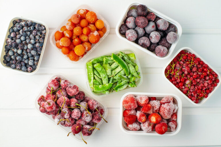 Frozen berries and vegetables in plastic boxes on white wooden background